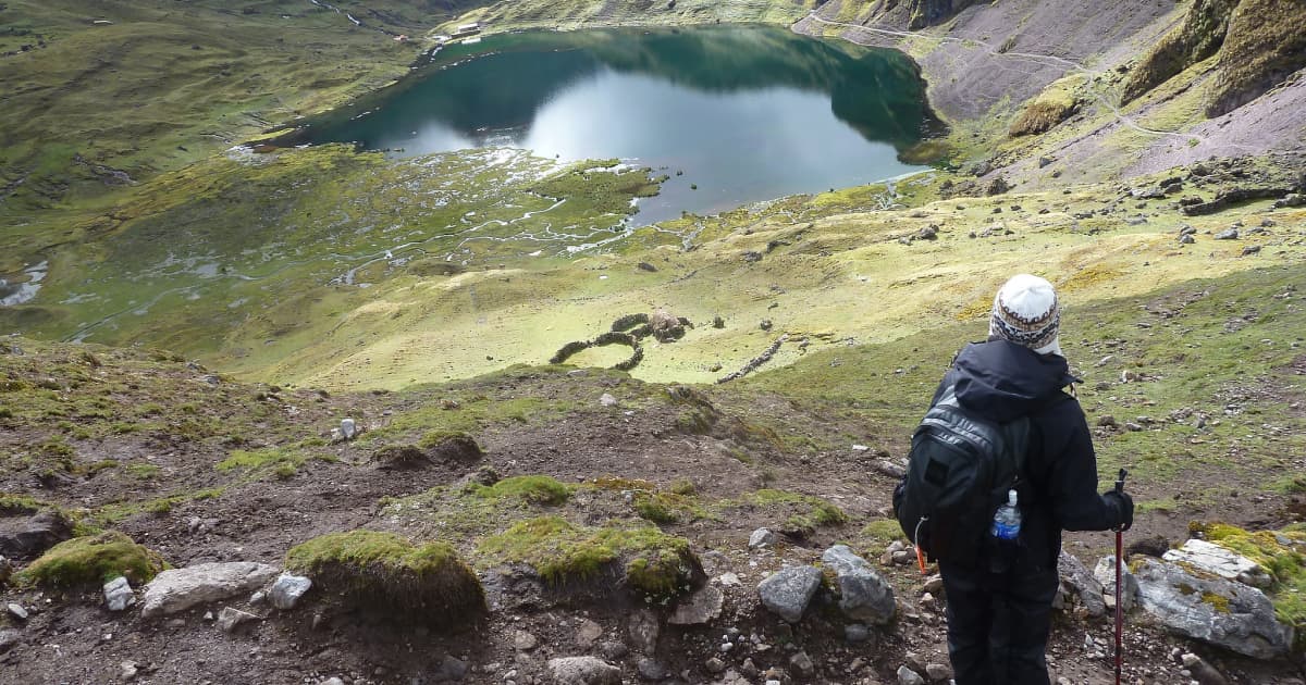 A hiker walking the lares trail overlooking a clear blue water pool