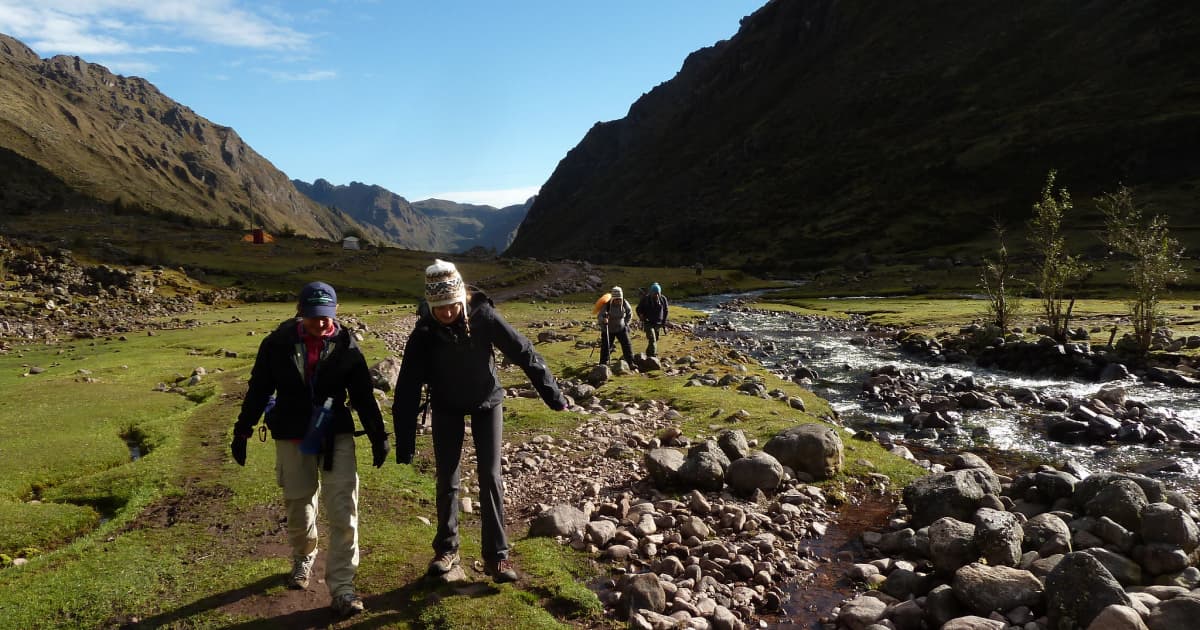 hikers walking along the flat rocky ground of the lares trek alongside a flowing lake