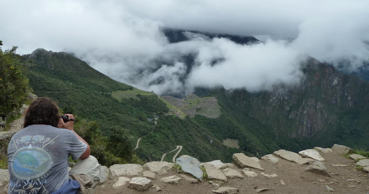 Traveler sitting on the edge of the Machu Picchu circuit taking pictures of the Machu Picchu ruins