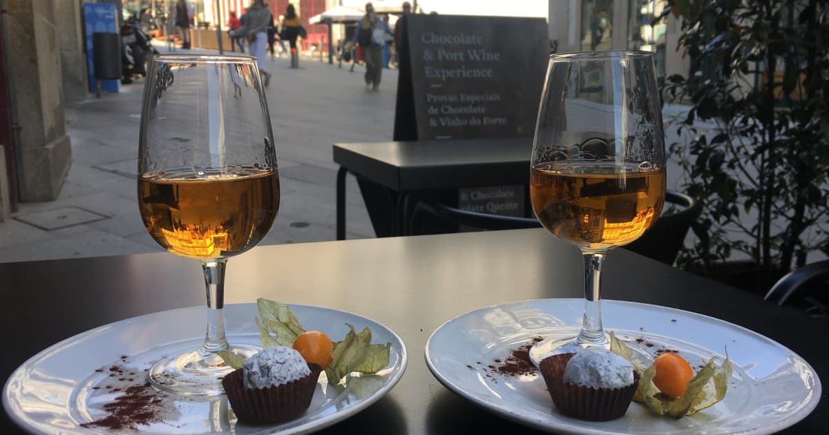 2 plates of desert and 2 glasses of wine with a small pathway down a city sidestreet in the background