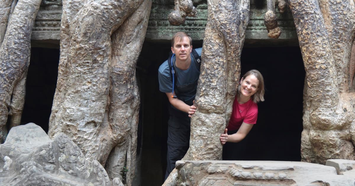 2 travelers posing by tree branches at Angkor Wat