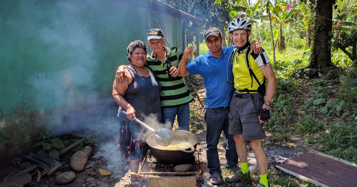 a local family welcoming a passing cyclists while cooking outdoors