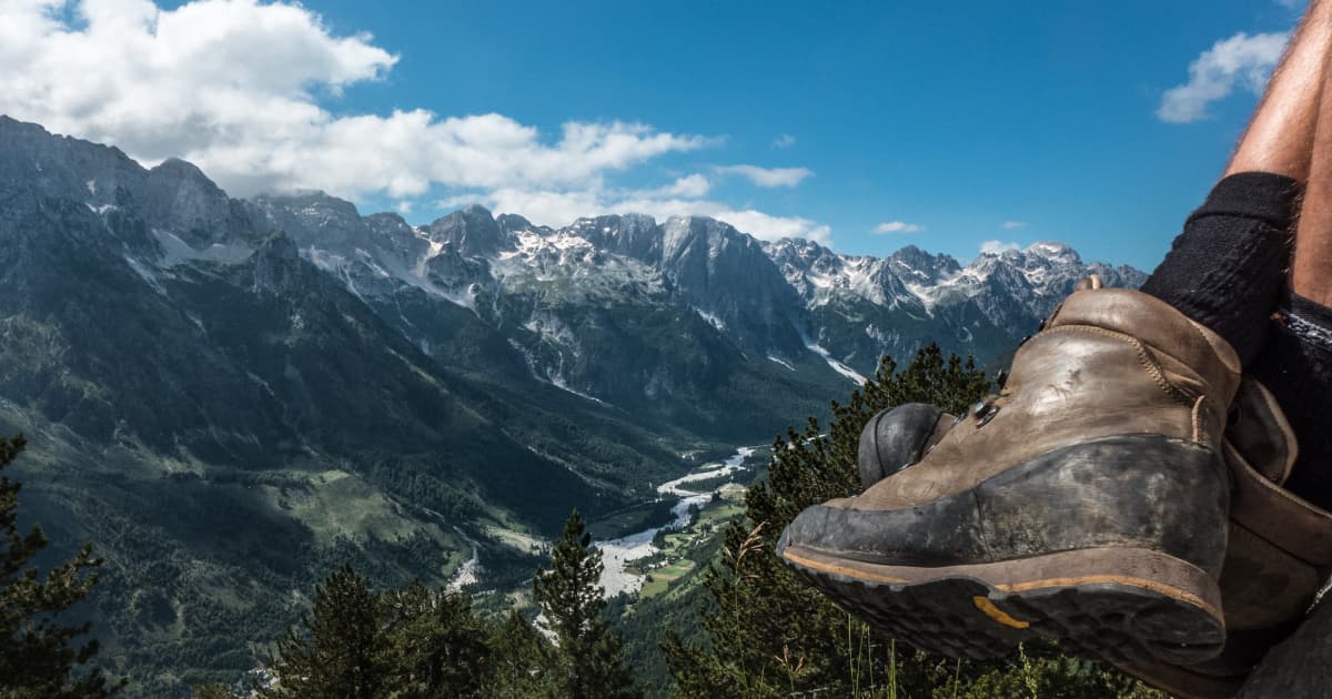 Close up of a hikers boot with a mountain range in the background on a sunny day with a blue sky