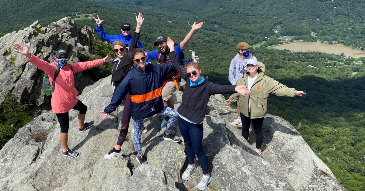group of hikers on a hilltop with arms outstretched celebrating the end of a hike
