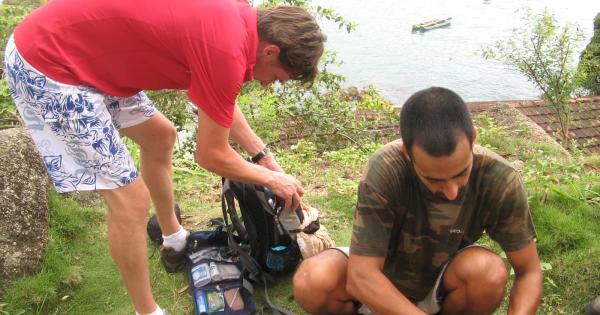 2 hikers checking their gear repair kits on the ground beside their backpacks