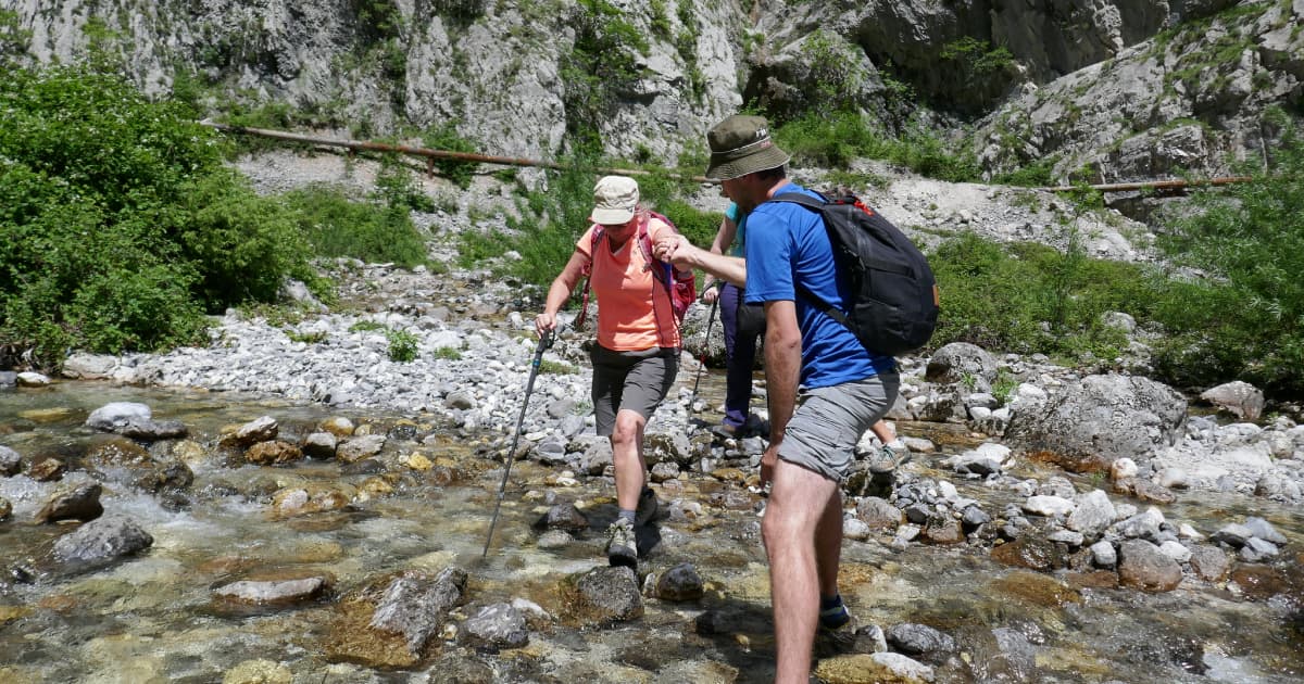 a man helping a woman over a small water pond on a hiking trail