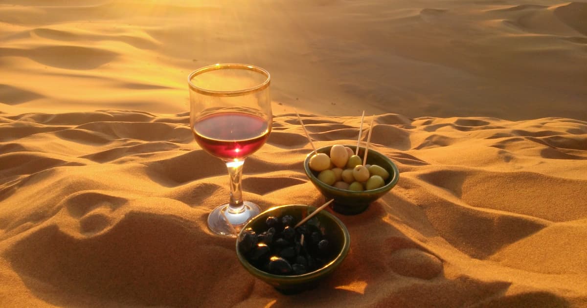 a glass of red wine and some olives in a bowl on sand dunes in Morocco