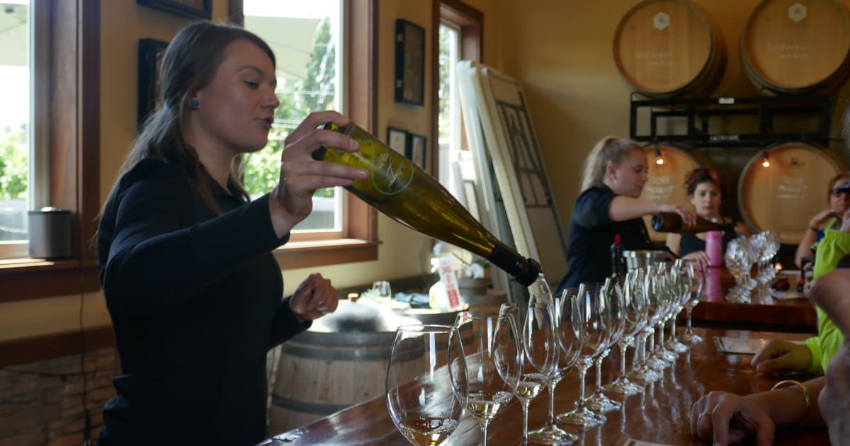 a girl behind a bar pouring red wine into a glass