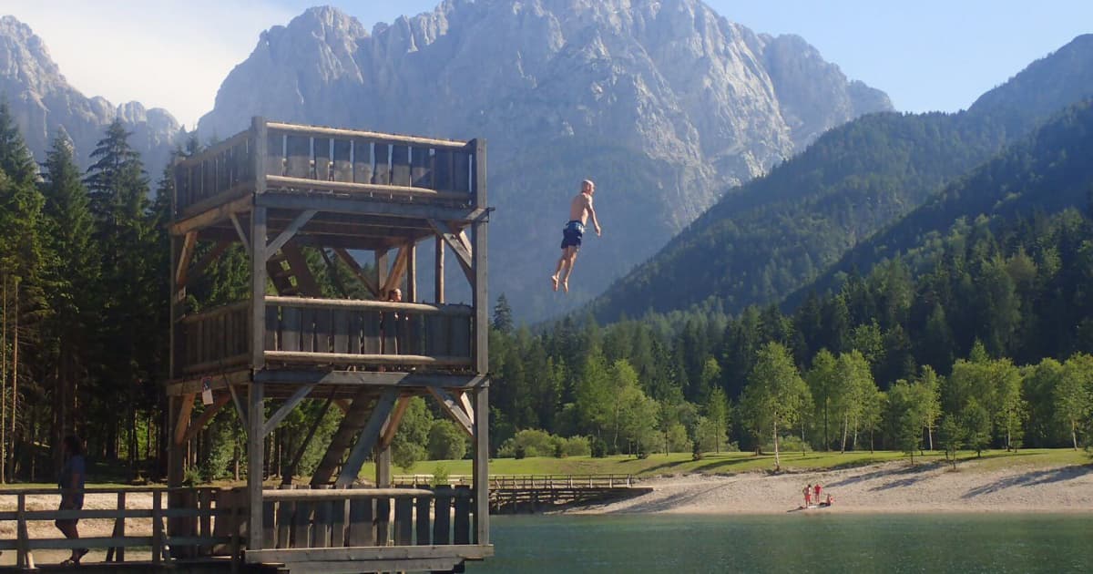A man jumping from a diving board into a lake with the backdrop of the Julian Alps in Slovenia