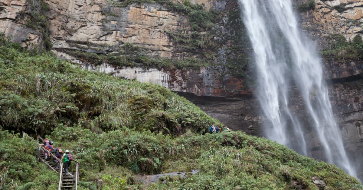 hiking through a trail in the Amazon rainforest in Peru with a waterfall flowing beside the trail