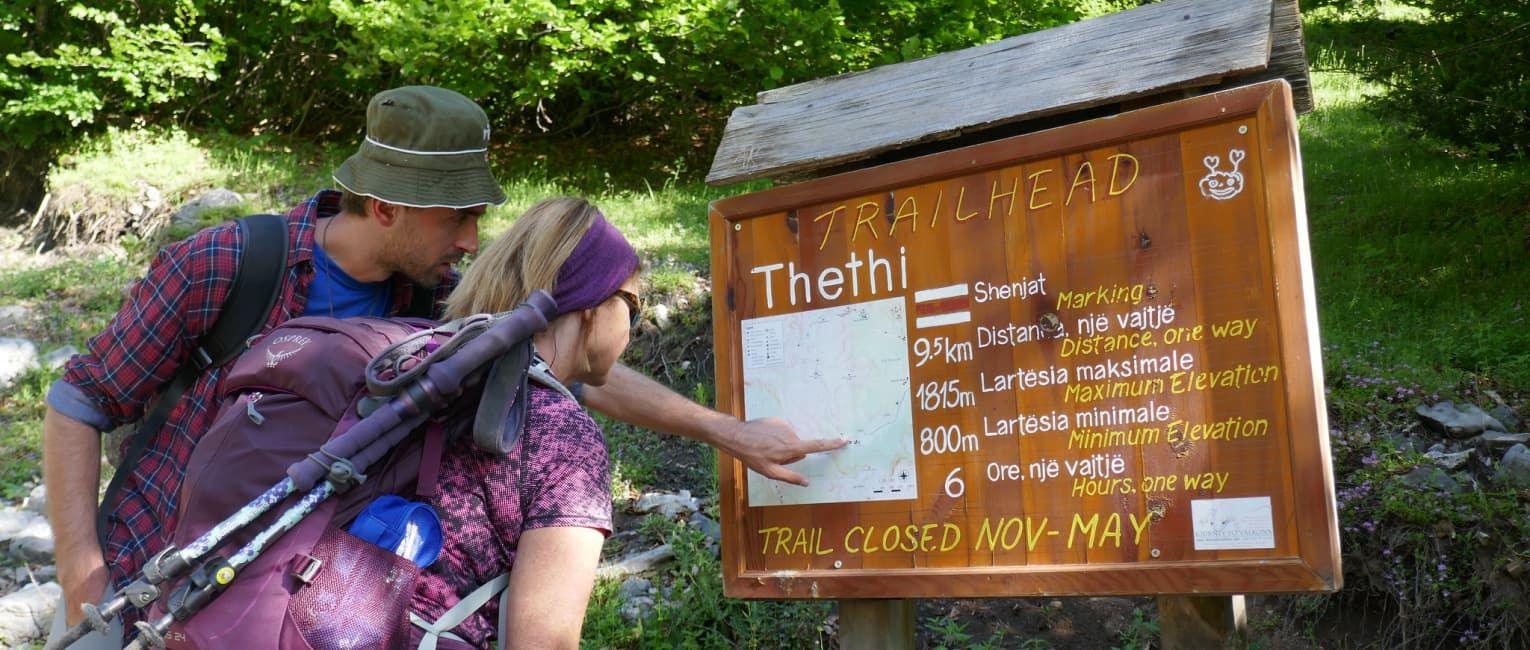 2 fully geared hikers checking out a map on a trail notice board