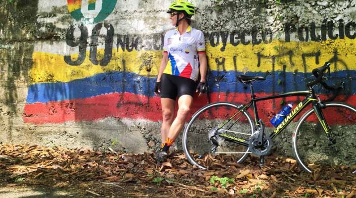Cyclist leaning against a wall painted with the flag of Colombia