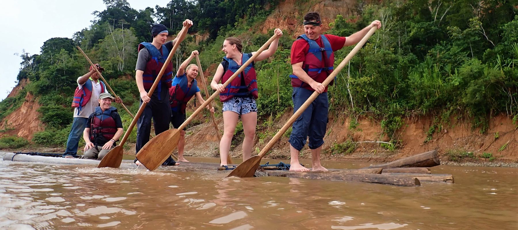 Group of travelers paddling down a lake on a board of logs