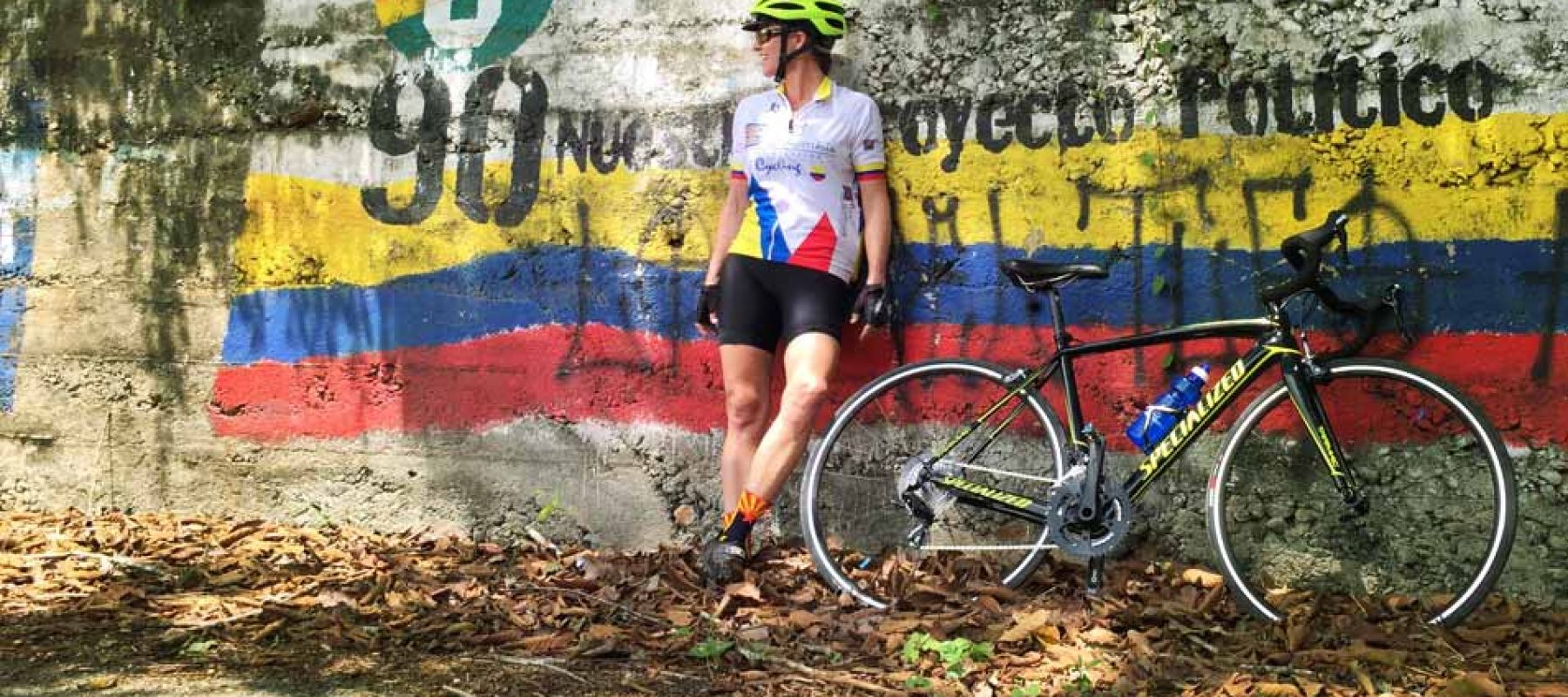 Cyclist leaning against a wall painted with the flag of Colombia